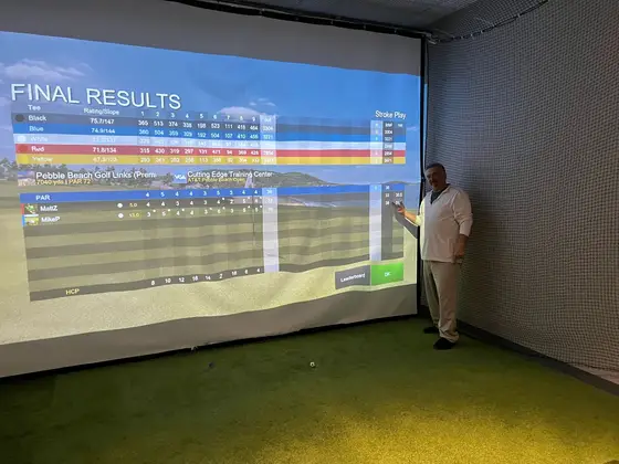Mike Pee pointing to the final results at Pebble Beach Golf Links on the simulator screen
