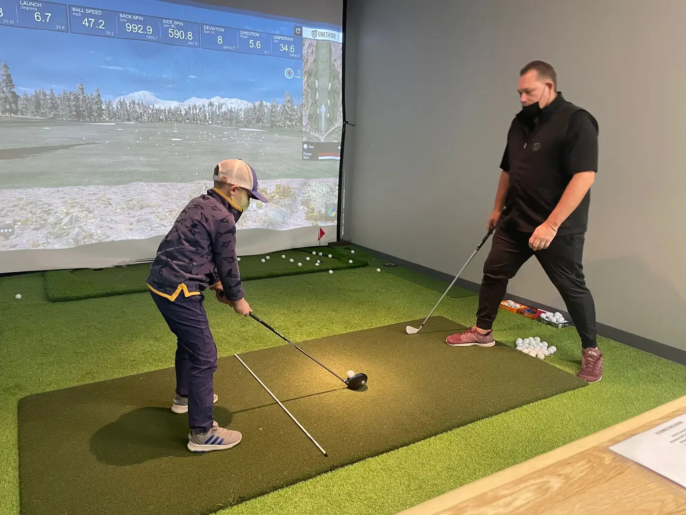 A young student addressing the ball while a coach watches from behind