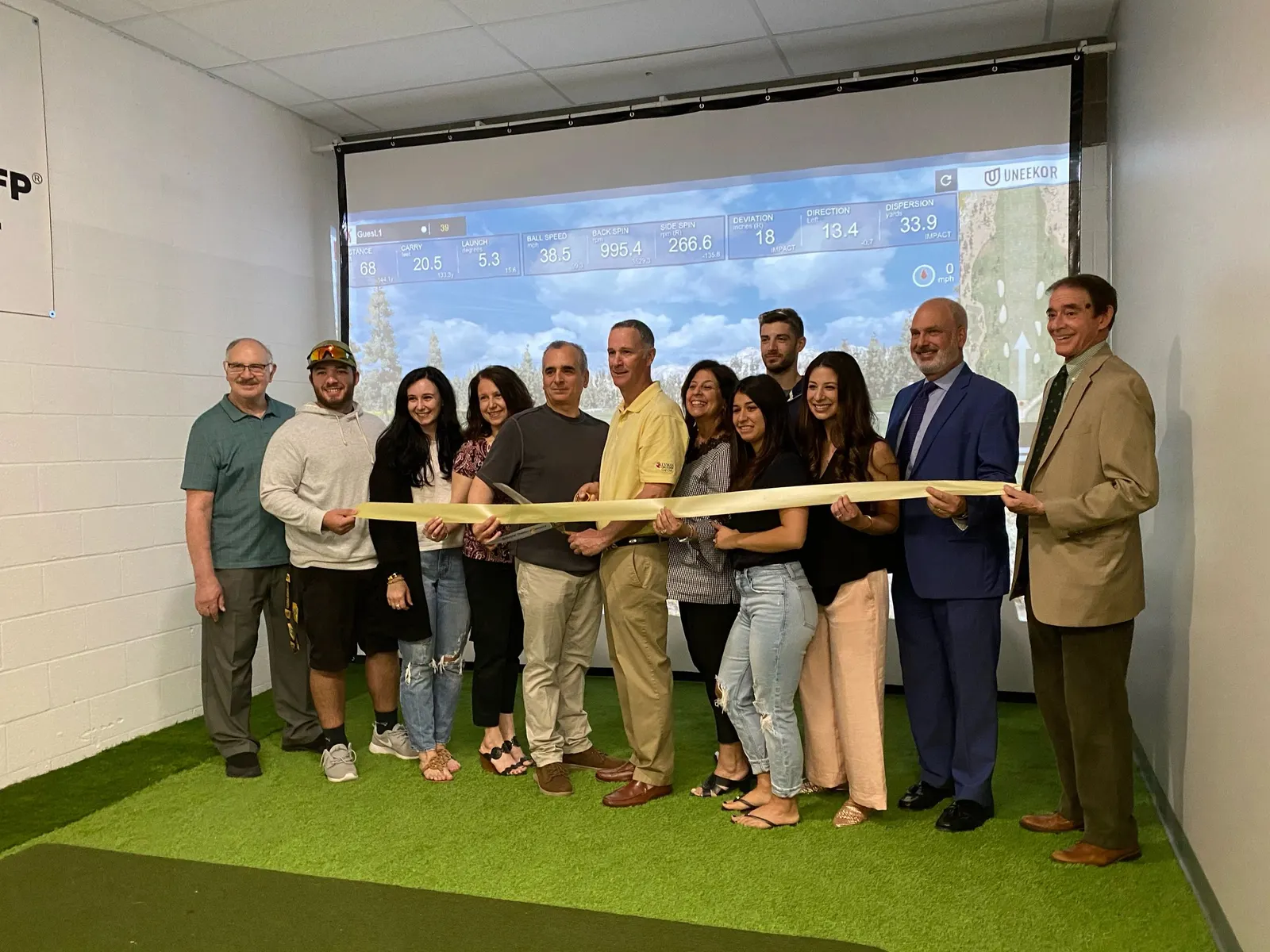 Owners, family and friends cutting the ribbon in front of the golf simulator screen